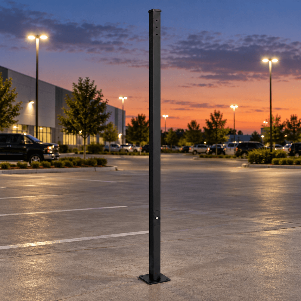 A 12' tall 4" x 4" straight square steel parking lot light pole, with a mounting arm drill pattern on one side, stands in an outdoor parking lot at dusk, with parking lot lights, trees, parked cars, and a colorful sunset sky in the background.